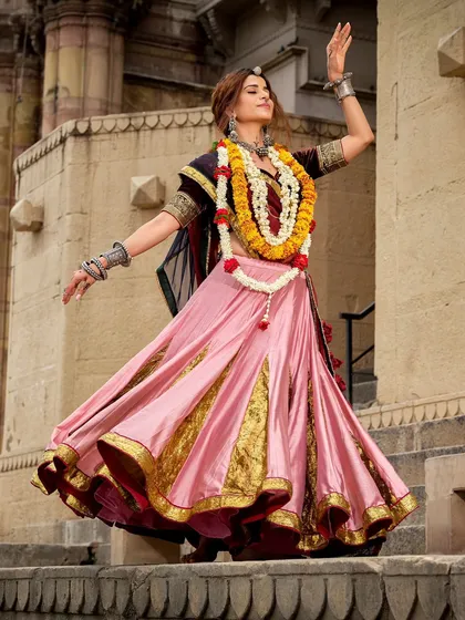 A dynamic shot from a Navratri campaign, capturing the model in a dance-like pose. The flowing pink lehenga, adorned with a floral garland, is styled to convey movement, joy, and the vibrant energy of the festival.