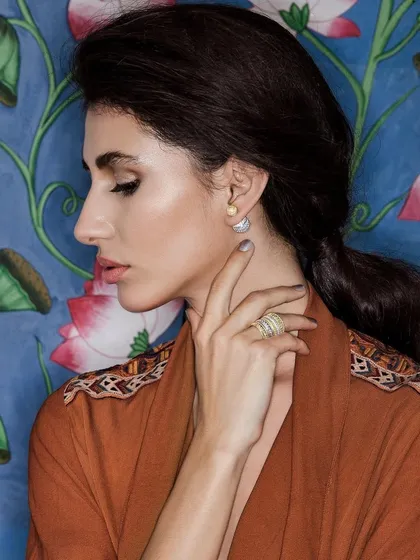 A beauty shot from a campaign for Amrapali Jewels, focusing on the elegant simplicity of the earrings and ring. The model's soft, side-profile pose and the warm, earthy tones of her wrap create a serene and sophisticated mood.
