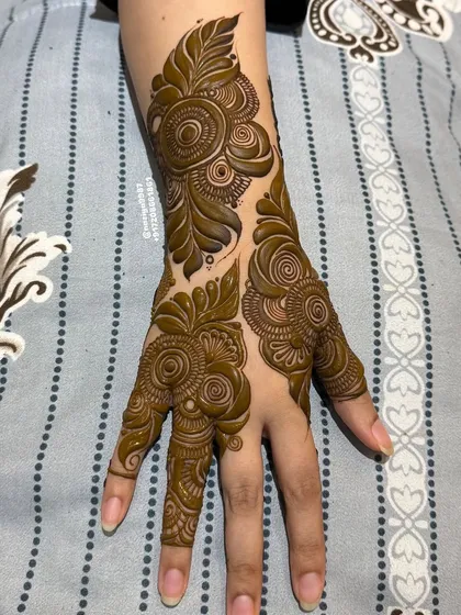 This is a perfect example of a simple yet elegant Gulf-style henna design. The focus is on bold, clean floral and leaf patterns with plenty of open skin, creating a striking and modern look on the back of the hand.