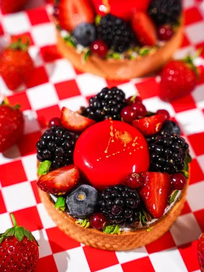 A close-up of a beautiful berry tart on a red and white checkered background. This classic American diner-style setup gives the sophisticated dessert a fun, retro twist.