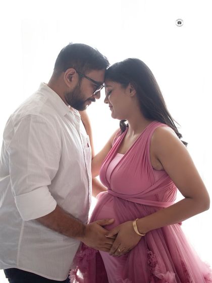 A close-up, intimate portrait of a couple. Their foreheads touching, they share a quiet moment, with the soft pink of her gown adding to the warmth.