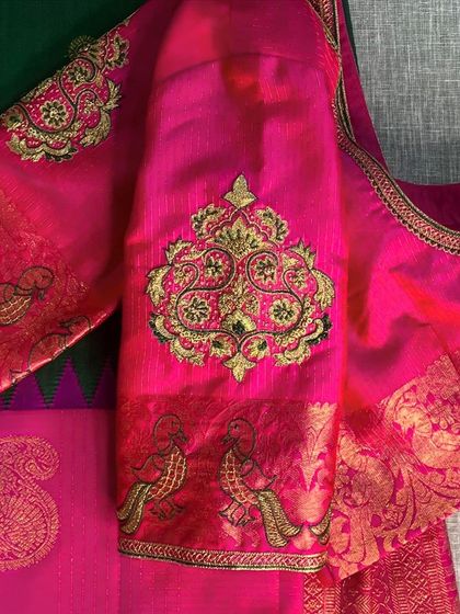 A vibrant pink Kanjeevaram saree blouse featuring a large, traditional motif embroidered on the sleeve, combining fabric from the saree border.