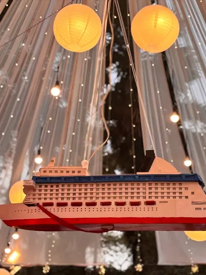 A unique decor element for a travel-themed or nautical-themed wedding. This model cruise ship hanging amidst lanterns adds a personalized and whimsical touch to the celebration.