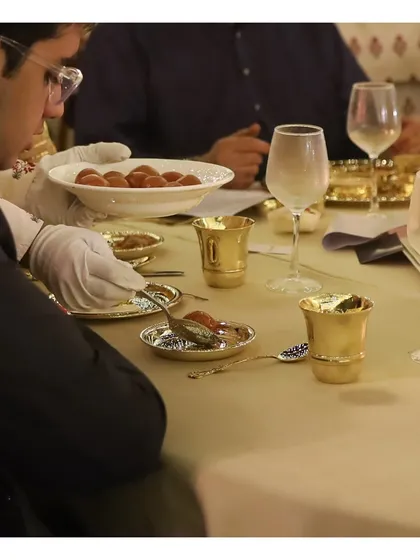Our server, in pristine white gloves, presents a traditional Indian dessert to a guest. This moment captures the essence of our silver service, where every dish is served with grace and precision, making each guest feel personally attended to.