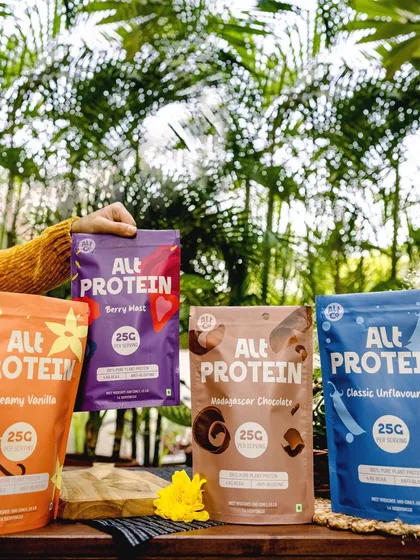 Showcasing the full range of Alt Co. protein powders. The outdoor, natural background reinforces the plant-based ingredients and healthy lifestyle association.