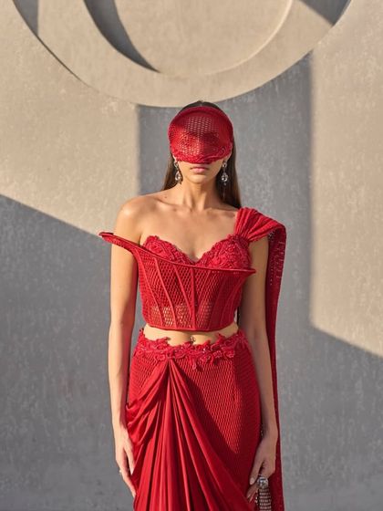 This sari transforms with every movement, fluid and luminous. A sheer mesh corset sculpts the silhouette, while the attached red drape flows like refracted light, embroidered with brilliance.