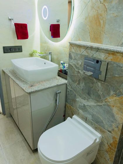 Another bathroom design showcasing a combination of grey marble tiles, a wall-mounted toilet, and an oval backlit mirror.