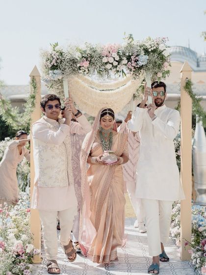 The bride makes her way to the mandap under a delicate floral canopy held by her brothers, a beautiful tradition incorporated into the ceremony.