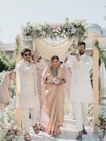 The bride makes her way to the mandap under a delicate floral canopy held by her brothers, a beautiful tradition incorporated into the ceremony.
