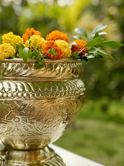 An intricately designed silver pot holding a mix of yellow and orange marigolds. This decorative piece combines traditional metalwork with fresh flowers for an elegant touch.