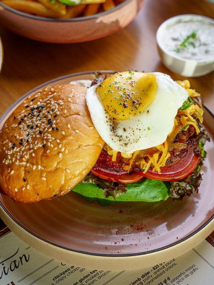A juicy burger topped with a perfect sunny side up egg. The composition is tight, focusing on the delicious combination of textures and flavors. This is a classic, irresistible burger shot.