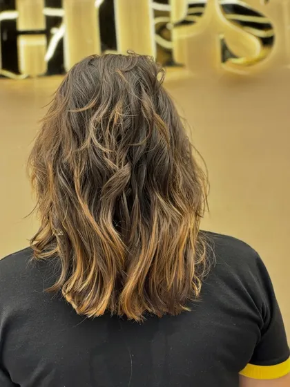 A beautiful hair color transformation on medium-length hair, styled with a messy, beach-wave texture for a modern and relaxed vibe.