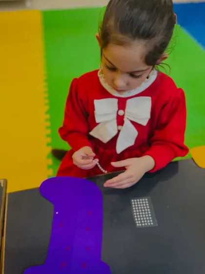 A young girl adds pearl-like decorations to her purple stocking craft.