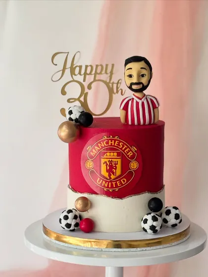 I designed this cake for a huge Manchester United fan's 30th birthday. It features the club's logo, a custom bobblehead-style figure of the birthday boy, and fondant footballs, all on a bold red and white buttercream cake.
