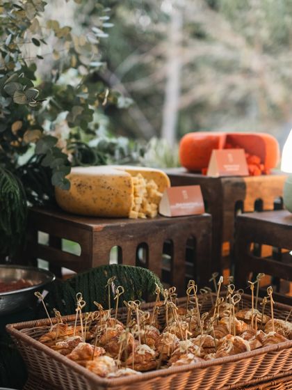 A detailed shot of the savory offerings on our grazing table, including a basket of pastries and large wheels of cheese, set against a backdrop of eucalyptus leaves.