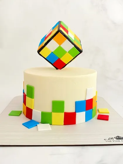 A mind-bending Rubik's Cube cake. The top features a fully solved cube, while the sides have colorful tiles, making it a perfect cake for a puzzle lover.