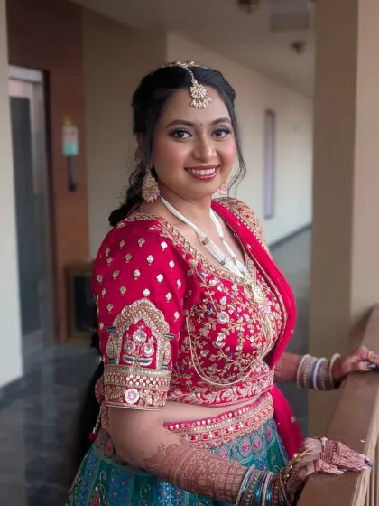 A happy Gujarati bride, ready for her big day. Her look features a vibrant red and teal lehenga, complemented by makeup that enhances her natural glow. The focus is on radiant skin and expressive eyes, perfect for a daytime wedding.