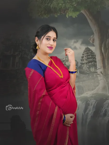 A beautiful studio portrait of a mother-to-be in a red saree, against an artistic backdrop with a temple silhouette.