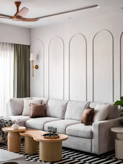 We designed this luxurious living room with a focus on creating a serene and sophisticated atmosphere. The large, comfortable L-shaped sofa is perfect for family time, and the wall is adorned with elegant arched mouldings. The organic-shaped wooden coffee tables and a striped rug add texture and warmth to the space.
