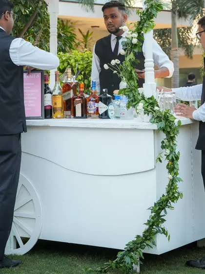 A charming white bar cart, decorated with a simple green garland, ready to serve guests at an elegant outdoor celebration.