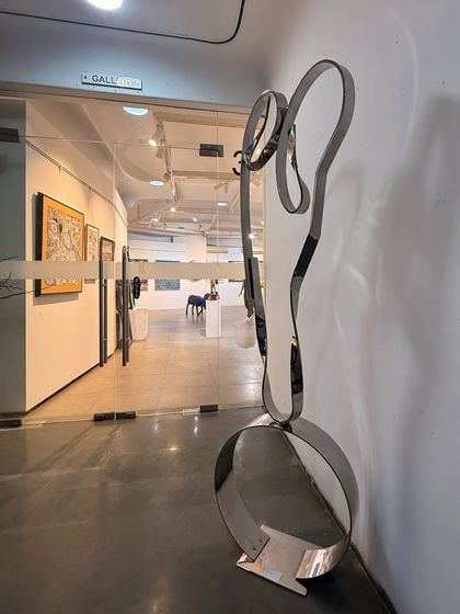 "The Bond" on display in a gallery. This view shows the full 78-inch height of the stainless steel and brass sculpture, highlighting its elegant and commanding presence.