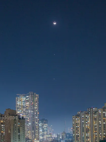 A clearer view of the planetary alignment, with the Moon, Jupiter, and Venus visible as bright points of light over Mumbai.