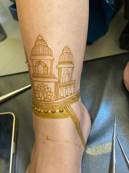 This is the 'before' shot, showing the fresh, natural henna paste for an architectural foot design. You can see the clean lines of the temple domes and the delicate beaded anklet detail.
