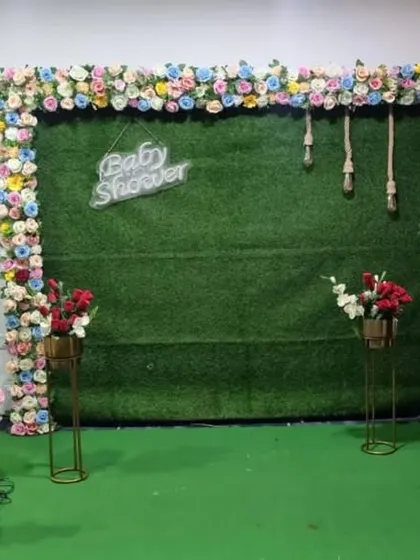An outdoor baby shower setup with a floral-bordered green backdrop and props for guests to enjoy.