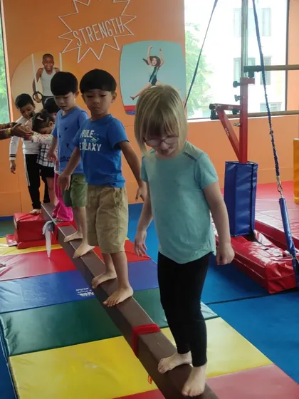 Children patiently wait their turn to walk across the balance beam, learning social skills like sharing and taking turns while practicing their physical skills.