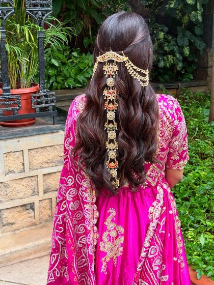 A stunning half-updo featuring an elaborate, cascading hair accessory. This is a perfect statement piece for a Mehendi or Sangeet, adding a touch of royalty to the look.