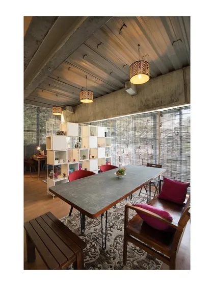 The main discussion table sits under the exposed decking of the floor above, showcasing the building's honest structural system. A modular shelving unit acts as a permeable screen, defining space without creating solid walls.