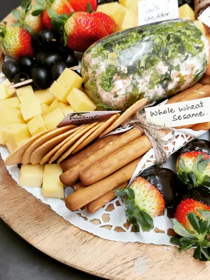 A look at one of our signature Cheese Platters, a perfect gift or centerpiece. This board includes a homemade herb cream cheese log, assorted cheese cubes, whole wheat sesame crackers, breadsticks, fresh fruit, and chocolate-dipped strawberries.