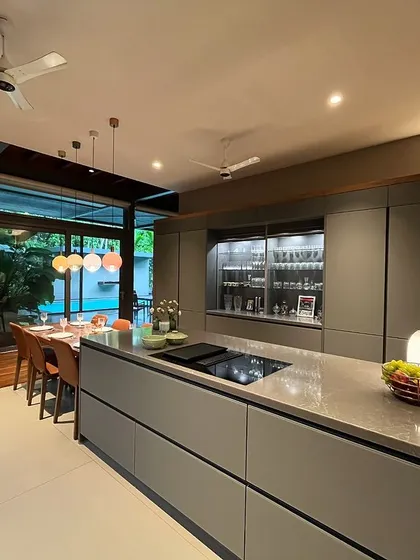 The kitchen island features an induction cooktop and overlooks the dining area and the home's lush green surroundings, making cooking a social and scenic experience.