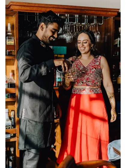 A fun, candid moment of the couple pouring drinks at a home bar during their pre-wedding festivities.