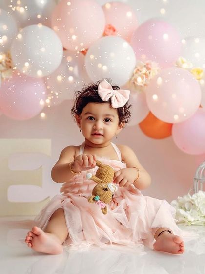A classic first birthday portrait, holding a little teddy bear amidst a beautiful balloon arrangement.