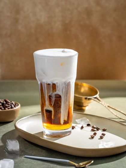 An iced coffee with a thick layer of cold foam cascading down the sides, creating a visually appealing texture.