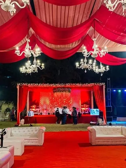 A grand reception setup with a red-themed stage and white lounge sofas for guest seating. The entire area is tied together with red carpeting and draping for a cohesive, royal look.