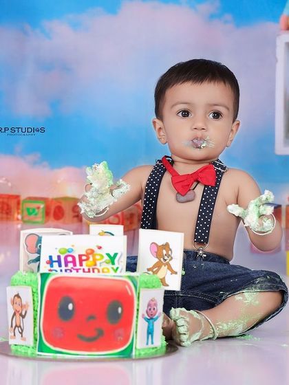 A close-up of the baby boy enjoying his Cocomelon cake. The frosting on his face and hands is a testament to a successful and fun cake smash.