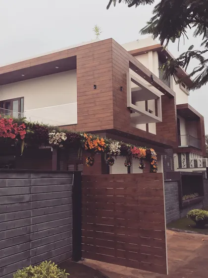 This is the daytime view of a contemporary bungalow we designed for an industrialist in Hubli. The facade combines wood-finish panels with clean white surfaces, while manicured shrubs line the perimeter, softening the modern architecture.