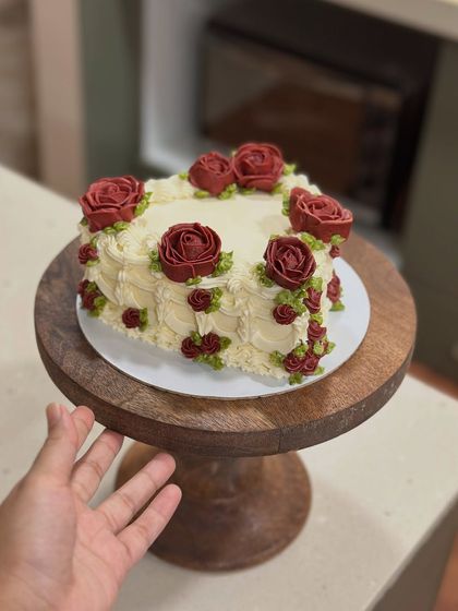 Holding up the finished heart cake on a wooden stand. It's a compact size, perfect for a special dinner or a small gathering.