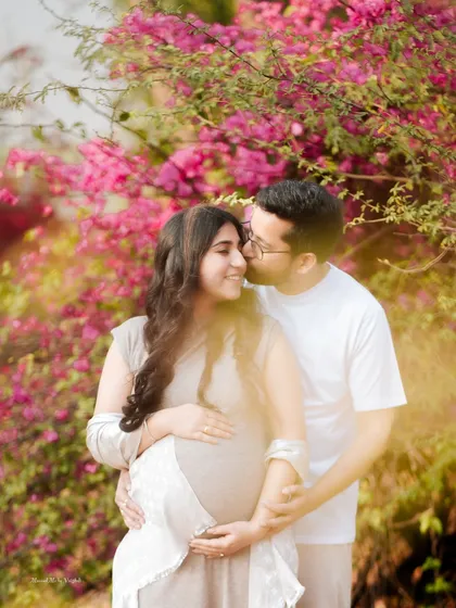 A romantic couple portrait set against a backdrop of vibrant bougainvillea. This outdoor pregnancy shoot highlights the beauty of nature and the couple's bond.