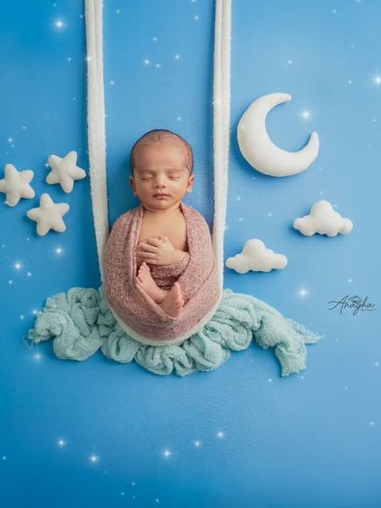 A fantasy-themed newborn photo showing a baby sleeping on a swing made of clouds, set against a starry blue night sky with a crescent moon.