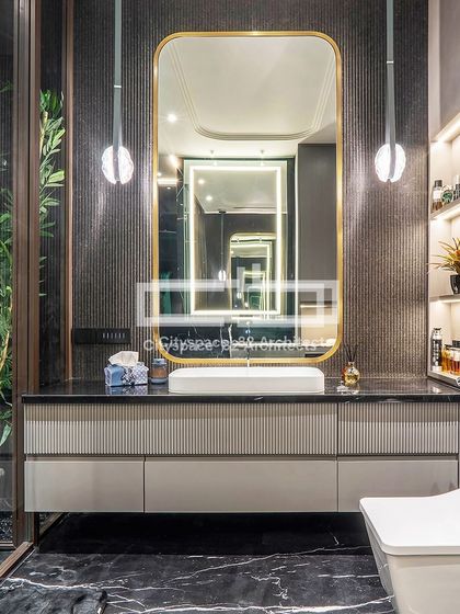 This bathroom design features a captivating vanity with a large, gold-framed mirror and spherical pendant lights. Vertical paneling adds texture and depth, while black marble floors and glass partitions complete the chic, high-end ambiance.