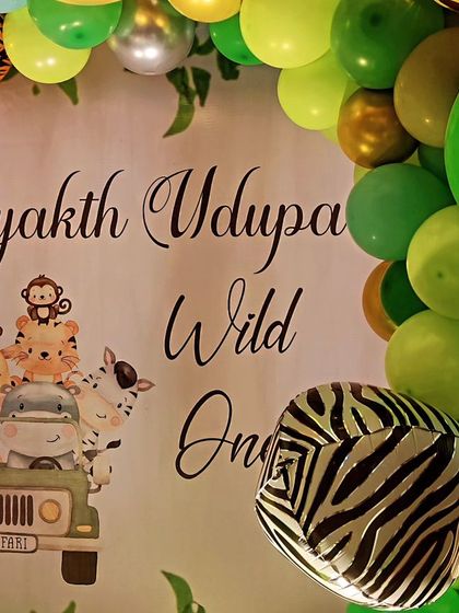 A close-up of a "Wild One" jungle theme backdrop, featuring cute cartoon animals and zebra-print foil balloons.