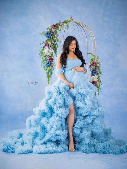A serene moment of reflection. The combination of the floral-adorned birdcage prop and the magnificent blue gown creates a truly enchanting and artistic scene.