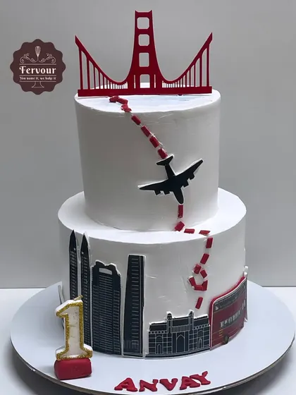 A travel-themed cake celebrating a journey from San Francisco to Mumbai for a first birthday. The design features the Golden Gate Bridge and the Gateway of India.