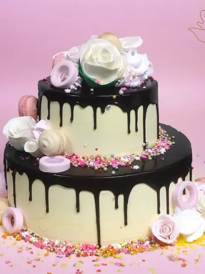 A stunning two-tier chocolate drip cake, decorated with macarons and roses. This beautiful and delicious cake is perfect for a wedding, anniversary, or milestone birthday.
