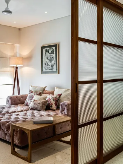 A comfortable, tufted daybed sits in a cozy nook, separated by a fluted glass and wood sliding door. This space in the Terrazzo Residence blends Japanese minimalism with contemporary Indian design for a relaxed feel.
