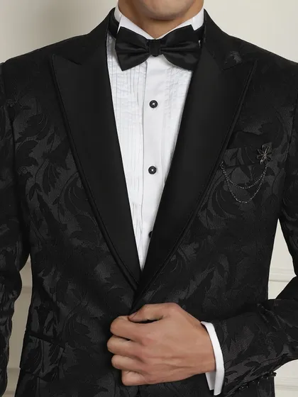 A close-up of the black patterned tuxedo, showing the texture of the jacquard fabric and the sharp black lapel.