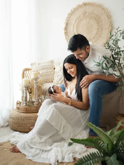 A wide shot of a new family in my bohemian studio setup. The natural elements and soft lighting create a warm and inviting atmosphere for newborn photography.